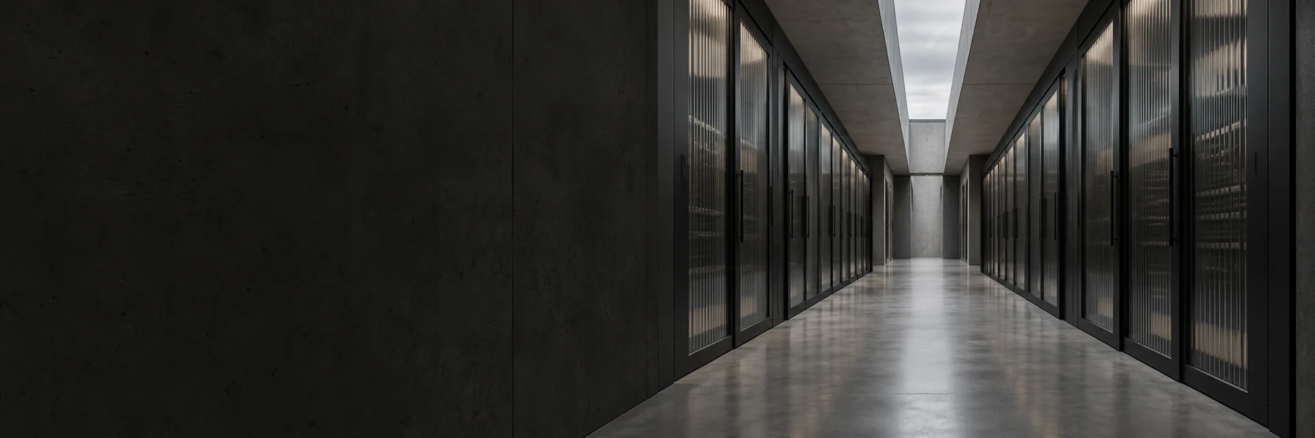 A concrete corridor lined with glass-fronted server cabinets under a skylight.